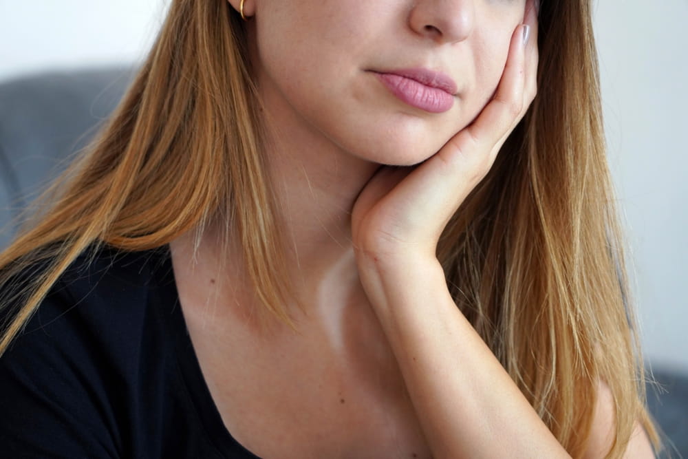 Une jeune femme avec la main sur la joue, car elle souffre de douleurs à la mâchoire associées au bruxisme